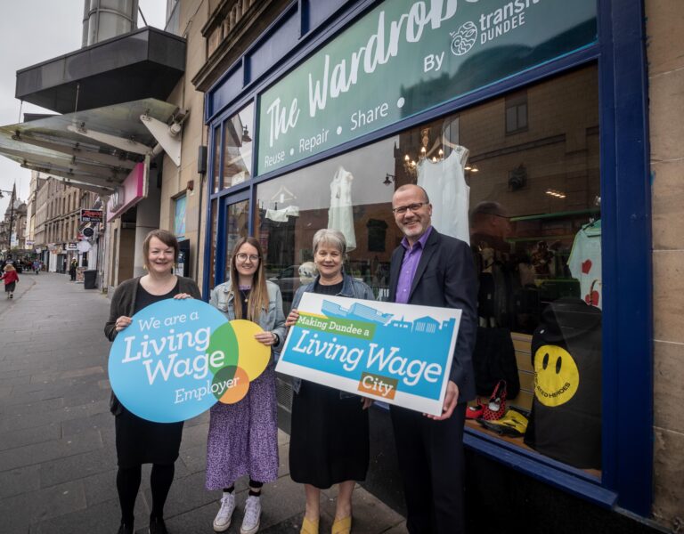 a group of people stand outside the wardrobe in Dundee City. They are holding Living Wage logo boards