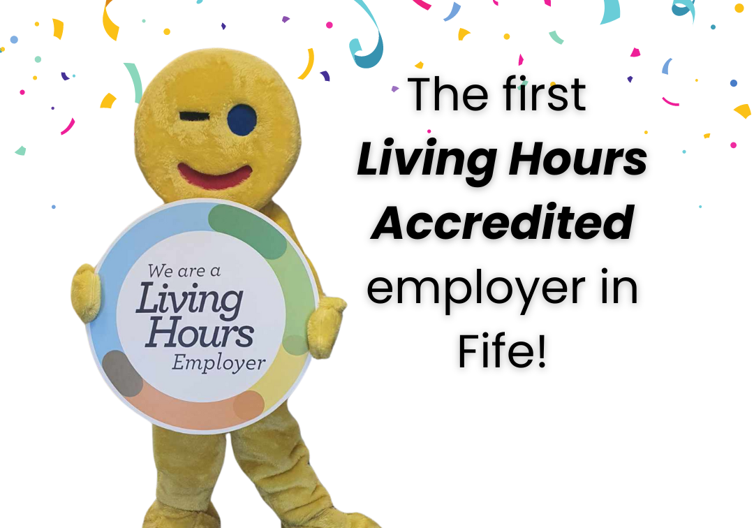 The Fife Gingerbread mascot, Gingey, stands holding a Living Hours logo board. Gingey is a human sized gingerbread man.