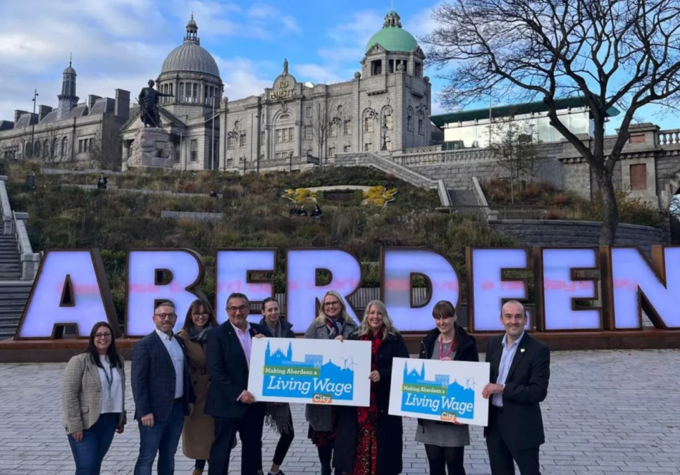 A group of employers stand in front of a large Aberdeen sign holding Aberdeen living places signs